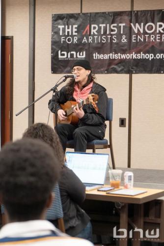 A workshop member plays guitar and sings an original song at The Artist Workshop: Auditions Round One.